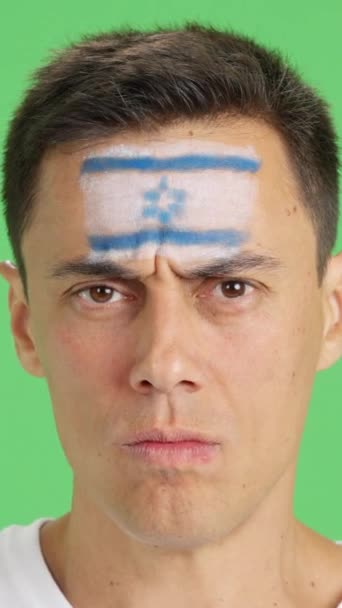 Film w studiu z chromą zbliżenia poważnego mężczyzny z izraelską flagą namalowaną na twarzy patrzącego w kamerę - Materiał filmowy, wideo