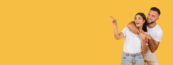 Lachende Millennial-Europäerin im weißen T-Shirt zeigt mit dem Finger auf den Kopierraum, isoliert auf gelbem Studiohintergrund, Panorama. Überraschung, Aufmerksamkeit, Verkauf - Foto, Bild
