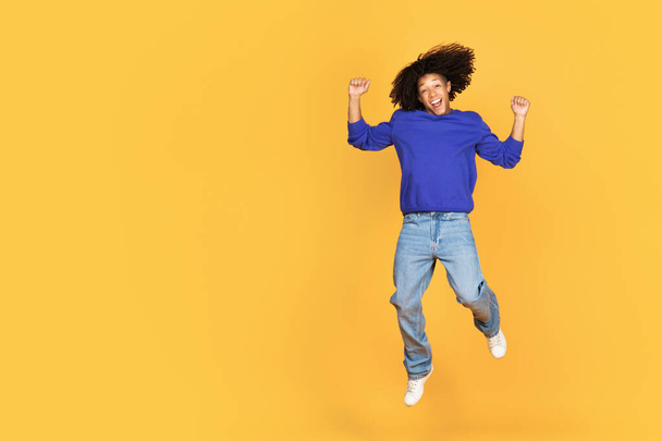 Freude über den Sieg. Emotionaler schwarzer Kerl springt in die Luft und gestikuliert Ja, glücklicher Afroamerikaner schüttelt Fäuste und schreit vor Begeisterung, hat Spaß auf gelbem Studiohintergrund, Kopierraum - Foto, Bild