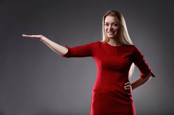 Haar gebaar is een van evenwicht en precisie, arm uitgestrekt in een strakke rode jurk om iets te presenteren - Foto, afbeelding