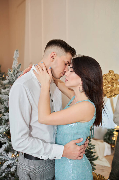 junges süßes hübsches verliebtes Paar küsst sich an Heiligabend in der Nähe des Baumes mit Geschenken zu Hause im Dezember. - Foto, Bild