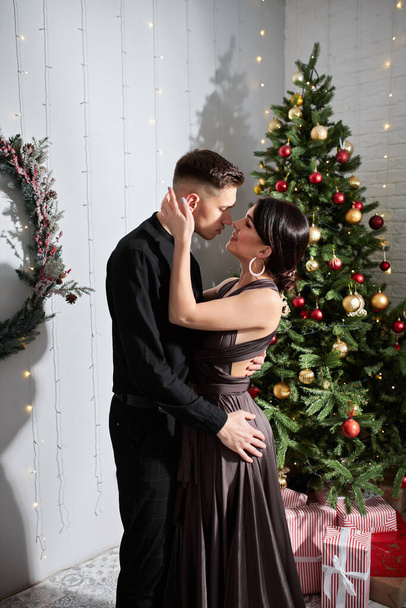 Giovane dolce bella coppia innamorata che si bacia nella vigilia di Natale vicino all'albero con regali a casa a dicembre
. - Foto, immagini
