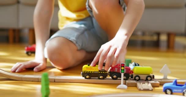 Un niño está jugando con un ferrocarril para niños. El niño juega con juguetes de madera en el suelo. Un tren de juguete monta en un ferrocarril de madera. Imágenes de alta calidad 4k - Metraje, vídeo