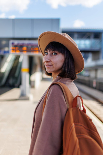 voyageant en train. Une jeune femme vêtue d'un manteau et d'un chapeau se tient à la gare et regarde l'horaire des trains. aventure et voyage. - Photo, image