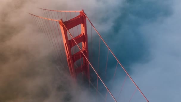 B roll motion achtergrond van magische mist wolk rond rode toren van Golden Gate brug in San Francisco, USA 4K. Adembenemende antenne van Golden Gate Bridge verlicht in gouden zon bij zonsondergang of zonsopgang - Video