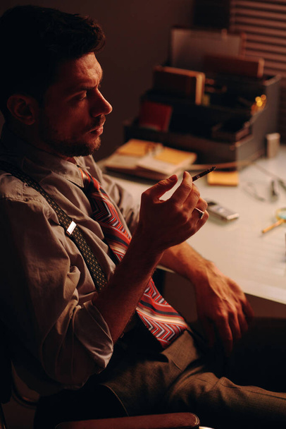 Boční pohled na mladého unaveného podnikatele s kouřící cigaretou v ruce sedí na pracovišti před kamerou a mají přestávku - Fotografie, Obrázek