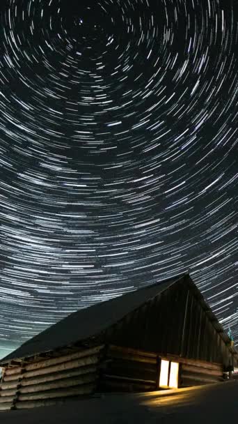 Время прохождения звездных троп в ночном небе, деревянный дом в горах зимой, звезды движутся вокруг полярной звезды, вертикальные кадры - Кадры, видео
