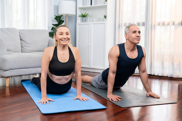 Szczęśliwa aktywna para w odzieży sportowej uprawiająca jogę na macie treningowej razem w domu. Zdrowy starszy mężczyzna i kobieta styl życia z ćwiczeniami jogi. Skutki - Zdjęcie, obraz
