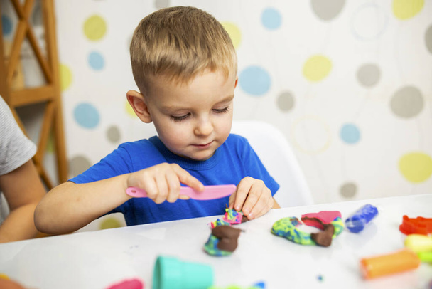 Küçük çocuk coşkuyla plasticinle oynuyor, evde beyaz masada hamur oynuyor, çocukların yaratıcılık kavramı. İnce motor becerilerin gelişimi - Fotoğraf, Görsel