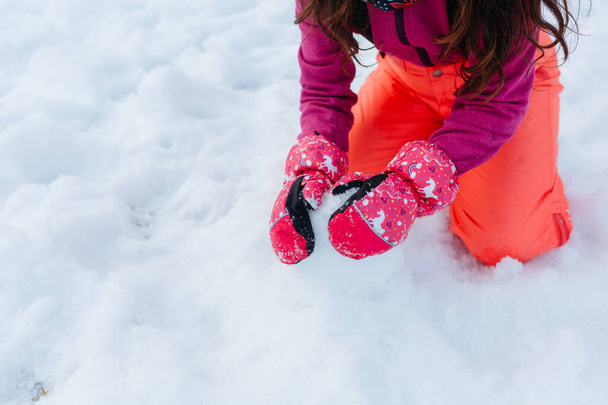 zblízka na ruce v rukavicích dívky v oranžových kalhotách hrát se sněhem - Fotografie, Obrázek