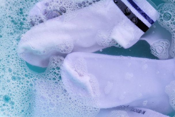 Calcetines blancos sucios empapados en agua, disolviendo detergente en lavabo azul. - Foto, Imagen