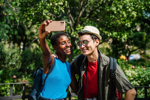 Coppia multiculturale di turisti che si fanno un selfie in un parco urbano - Foto, immagini