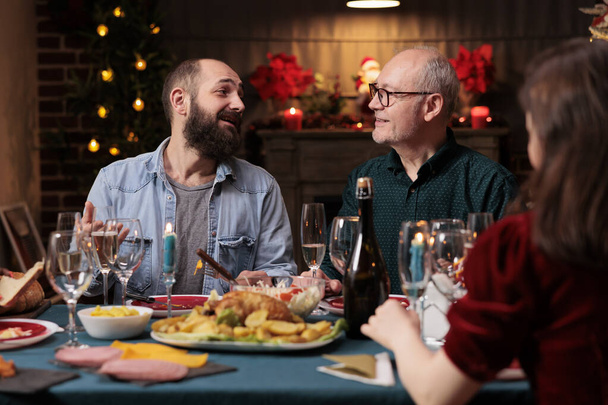 Eine Gruppe von Menschen trifft sich an Weihnachten, um gemeinsam ein festliches Abendessen zu feiern, saisonale Dezemberferien. Jung und Alt freuen sich am Tisch bei traditionellem Essen und Wein. - Foto, Bild