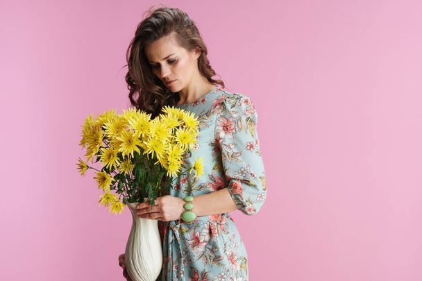 young female with long wavy brunette hair with yellow chrysanthemums flowers in vase against pink background. - Fotoğraf, Görsel