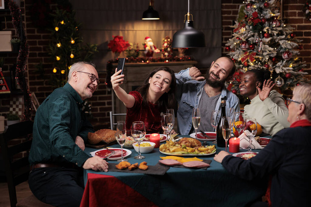 Família tirando fotos no jantar de Natal com deliciosa comida e copos de vinho, fazendo memórias durante o evento de férias de dezembro. Pessoas diversas se divertindo com fotos no smartphone em casa. - Foto, Imagem