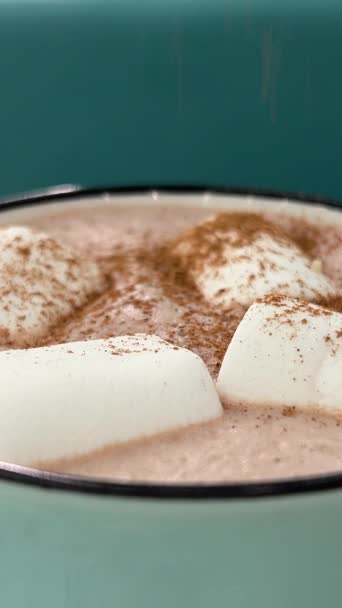 Kakao mit Marshmallows bestreut mit Zimt Grüne Tasse. Azurblauer Hintergrund köstlicher Heißer Kakao mit Marshmallows im Keramikbecher umgeben von winterlichen Dingen. Konzept für gemütlichen Urlaub und Neujahr. - Filmmaterial, Video