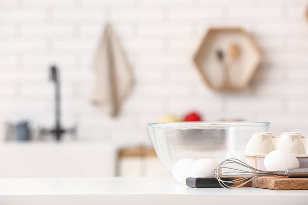 Paquet avec oeufs, fouet et bol en verre sur la table dans la cuisine - Photo, image