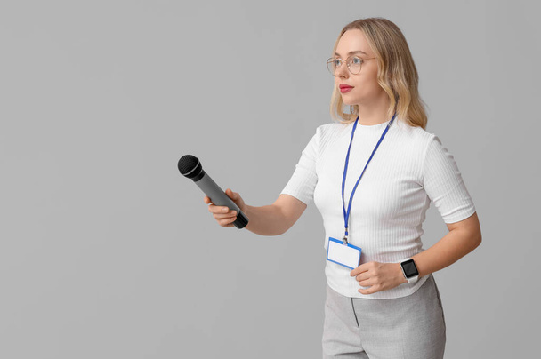 Portret van vrouwelijke journaliste met microfoon neemt interview op grijze achtergrond - Foto, afbeelding
