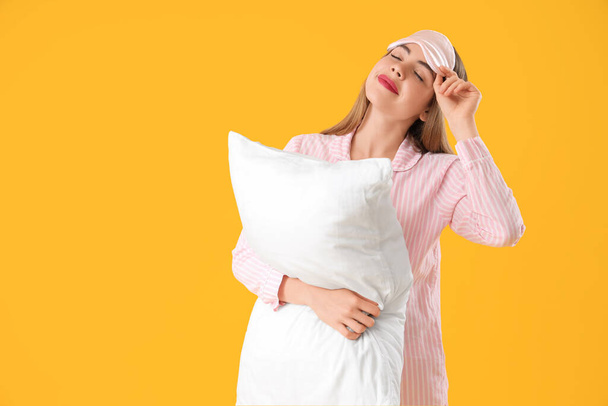 Портрет красивої молодої жінки в піжамі з подушкою на жовтому тлі - Фото, зображення