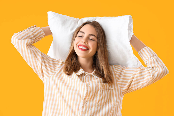 Portrait de jolie jeune femme en pyjama avec oreiller sur fond jaune, gros plan - Photo, image