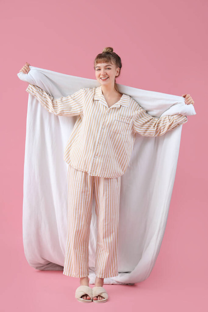 Portrait of pretty young woman in pajamas with blanket on pink background - Photo, Image