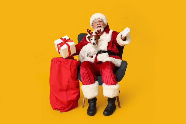 Santa Claus with cute Jack Russell Terrier dog in reindeer horns and bag on yellow background - Photo, Image