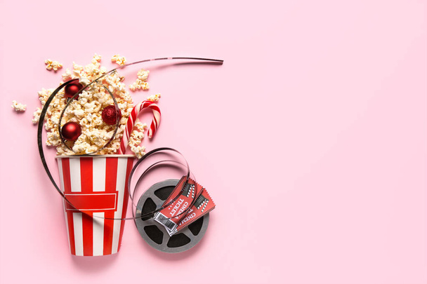 Bucket of popcorn with film reel, cinema tickets and Christmas decor on pink background - Photo, Image