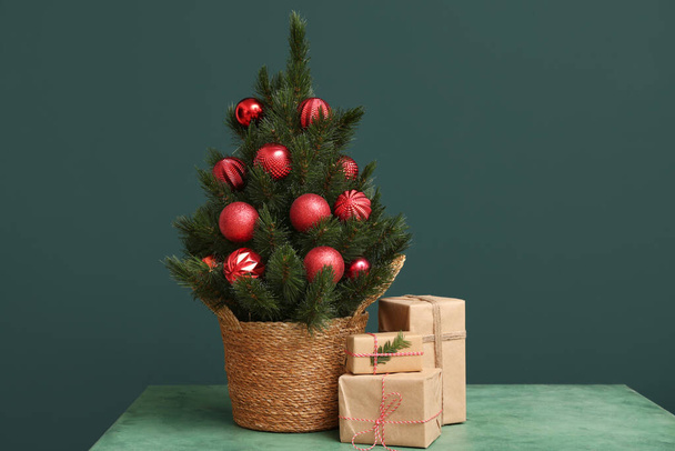 Красивая елка в горшке с подарками на столе на темно-зеленом фоне - Фото, изображение
