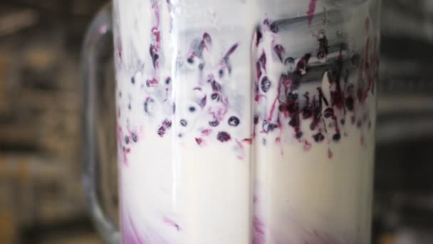 Preparación de un batido de frutas o batido de leche rosa en una batidora bayas de primer plano frutas que caen batido púrpura mezcla en la batidora eléctrica. Top view granada de fresa de arándano cayó en bebida jugosa - Imágenes, Vídeo