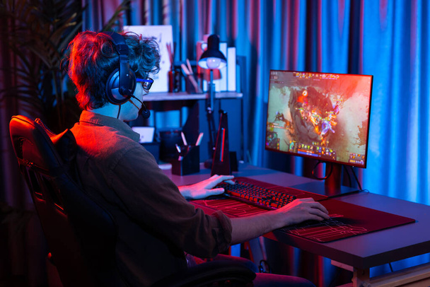 Host channel of young gaming streamer playing fighting Moba at battle arena game with multiplays team, wearing headphone on pc monitor with back side image at neon digital light modern room. Gusher. - Photo, Image