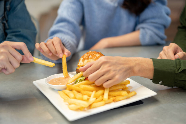 Imagem de close-up de amigos alegres gostando de comer batatas fritas em um café juntos, sair e almoçar juntos. Conceitos de amigos e alimentos - Foto, Imagem