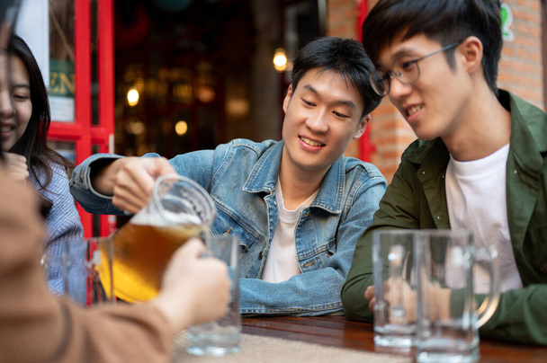 Щасливий молодий азіатський чоловік виливає пиво з баночки для своїх друзів, насолоджуючись висінням у ресторані або барі в місті разом. Концепція стилю - Фото, зображення