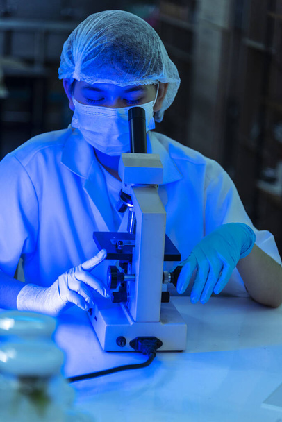 Vertikalwissenschaftlerinnen im Labor betrachten ein wissenschaftliches Mikroskop medizinischer Test zur Erforschung der Biologie Chemie mit blauem hellschwarzem Hintergrund. Männliche Techniker Labor analysieren Chemie Medizinische Forschung - Foto, Bild
