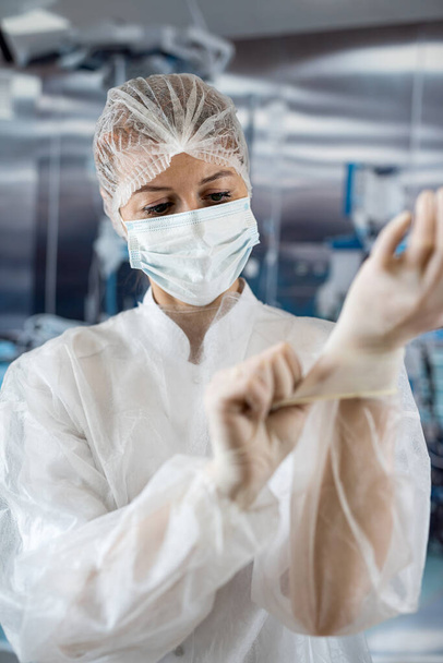 γυναίκα γιατρός φορούν παλτό βάζοντας αποστειρωμένα γάντια στο χειρουργείο. Εργάτης φροντίδας. Ιατρική έννοια - Φωτογραφία, εικόνα