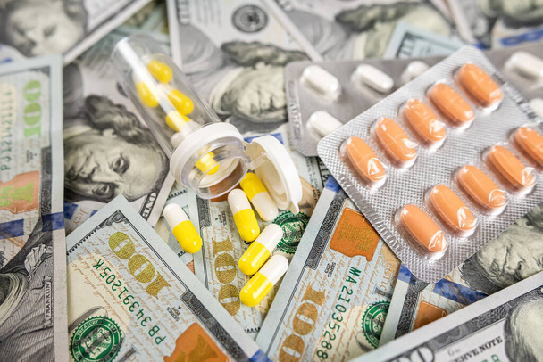 Unterschiedliche medizinische Pillen, verstreut auf Dollarpapiergeld als Hintergrund. Teure Medizin und Gesundheitskonzept - Foto, Bild