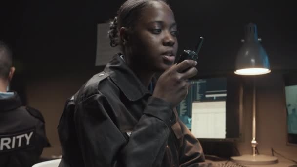 監視室のウォルキー・トーキーで同僚と話す若い黒人女性警備員の中型ショット - 映像、動画