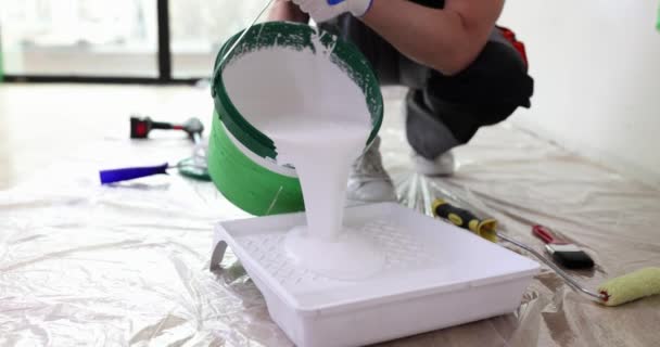 Männliche Reparaturarbeiter gießen weiße Farbe aus Eimer in Palette Nahaufnahme 4k Film Zeitlupe. Malerarbeiten Reparatur von Wohnungen und Häusern Konzept - Filmmaterial, Video