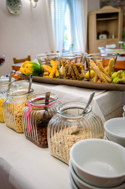 View of a hotel breakfast buffet featuring an enticing selection of various cereals and flakes. The vibrant array showcases a tempting assortment, from wholesome oats to crispy cornflakes - Photo, Image