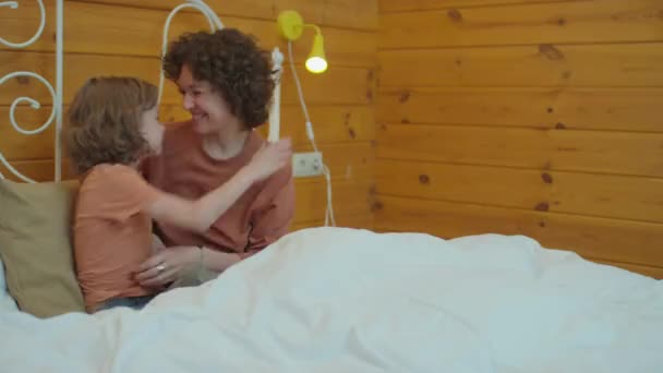 Mediana toma de la madre sentada en la cama abrazando a su hijo, teniendo momento de unión - Metraje, vídeo