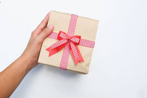 ένα πουλί 's eye view of photo woman Asian hands holding of craft paper gift box with red corp bow isolated on a white backdrop. Πρωτοχρονιά, Χριστούγεννα, Ημέρα του Αγίου Βαλεντίνου έννοια - Φωτογραφία, εικόνα