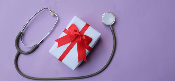 медичний стетоскоп з подарунковою коробкою ізольовано на фіолетовому пастельному тлі. концепція Різдво і Новий рік.горизонтальна фотографія - Фото, зображення