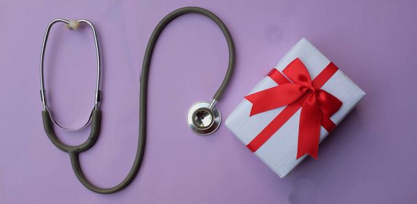 estetoscopio médico con caja de regalo aislada sobre un fondo pastel púrpura. concepto de Navidad y año nuevo.foto horizontal - Foto, imagen