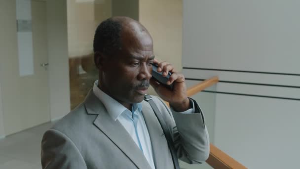 Στήθος μέχρι slowmo πλευρά του Μαύρου εκτελεστικού σε γκρι κοστούμι μιλώντας στο τηλέφωνο με τον επιχειρηματικό εταίρο στο διάδρομο γραφείο - Πλάνα, βίντεο