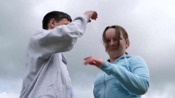 Komischer Kampf von Teenagern, Teenager-Mädchen schlägt einem Mann auf die Schulter, ein junger Mann stößt einer jungen Frau in den Kopf, einen Schlag auf die Stirn, lacht, reißt Arme gegen den Himmel, Sportbekleidung. Flirten - Filmmaterial, Video