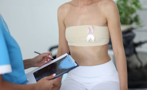 Доктор-маммолог держит рентген в буфере рядом с пациентом с перевязанной грудью в клинике крупным планом. Борьба с раком груди. - Фото, изображение