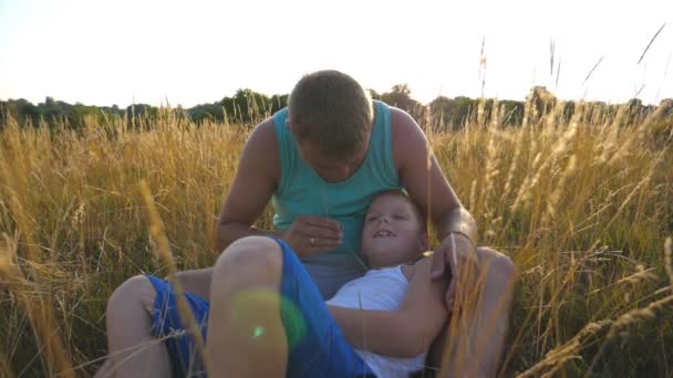 Otec, lechtání jeho malého syna venkovní. Šťastný mladý muž ležící na trávě na pole a hrát si s jeho chlapeček. Veselá a tatínek a jeho dítě baví spolu v parku. Zpomalené Detailní záběr. - Záběry, video
