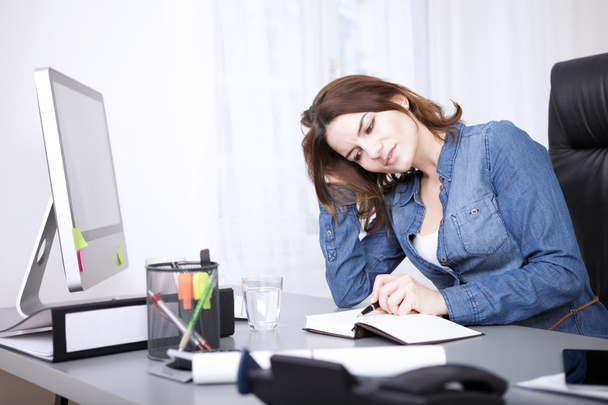 Бізнес-леді читає книгу з ручкою за столом
 - Фото, зображення