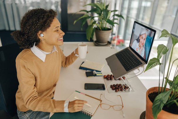 Nainen freelancer on video konferenssi asiakkaan kanssa ja tehdä muistiinpanoja istuu viihtyisä coworking - Valokuva, kuva