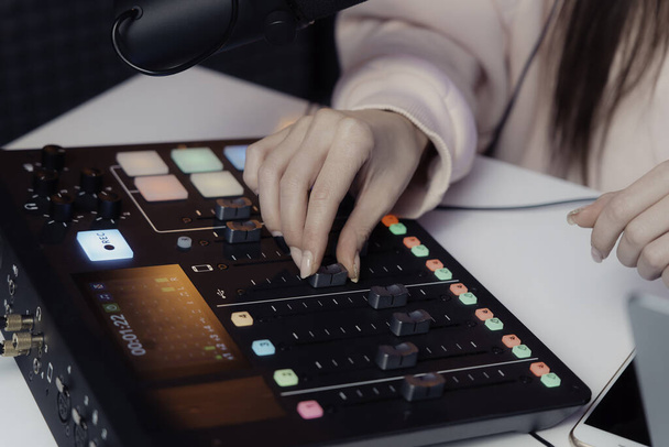 Close-up van een podcaster handen als ze vakkundig past een audio mixer, fine-tuning het geluid voor een live podcast opname - Foto, afbeelding