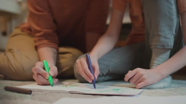 Focus selettivo medio primo piano di madre e figlio irriconoscibili seduti sul pavimento in camera da letto a disegnare immagini colorate con pennarelli - Filmati, video
